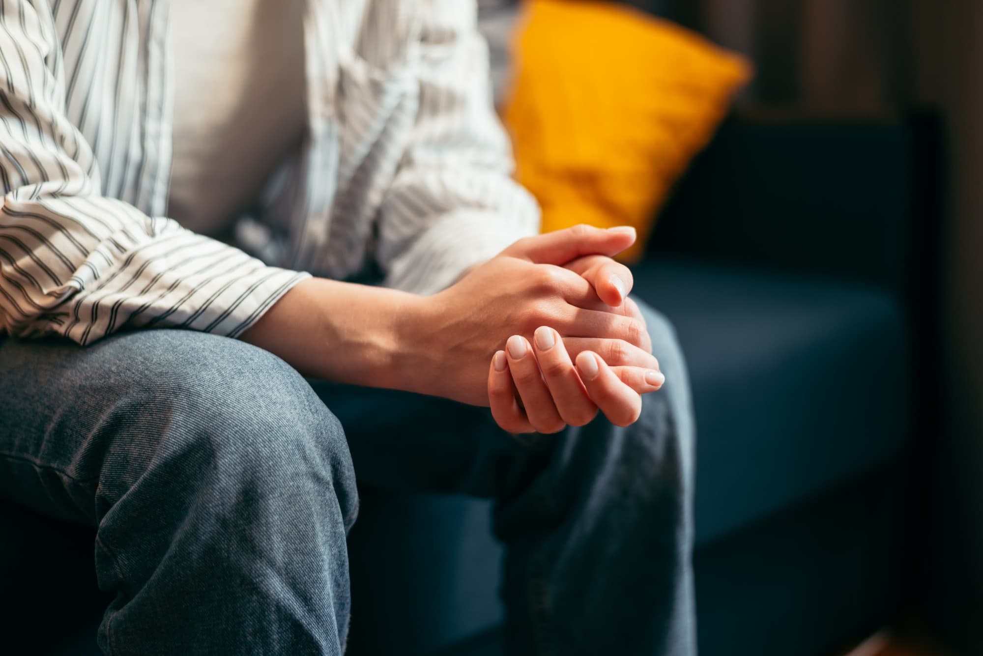 Person seated on a sofa with hands clasped over their knee