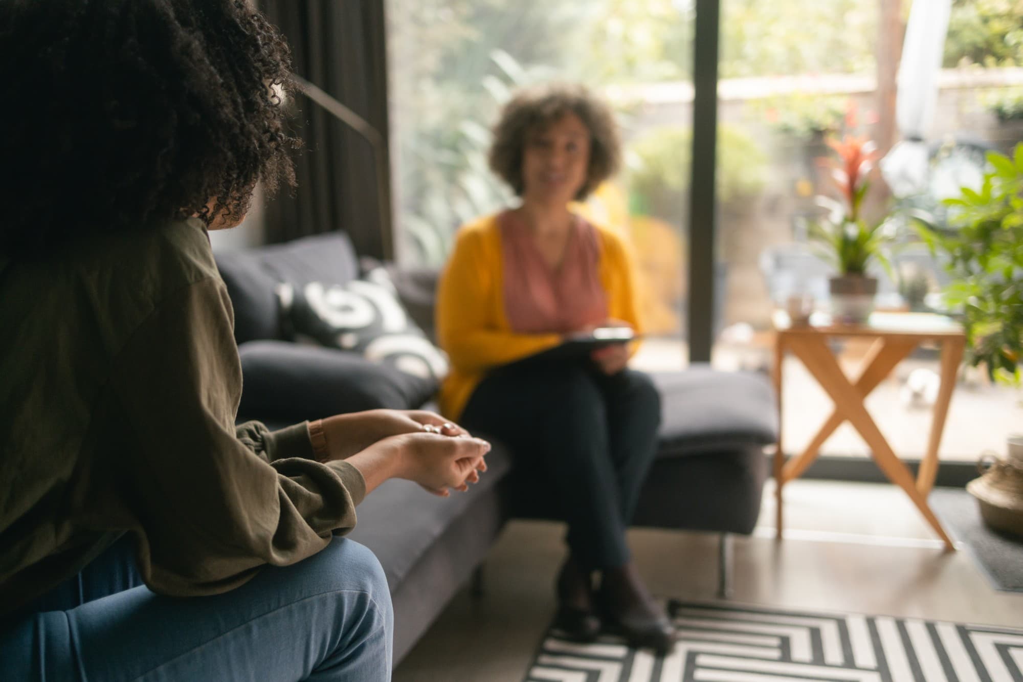 Woman on a sofa talking with a professional who holds a clipboard in a bright living room